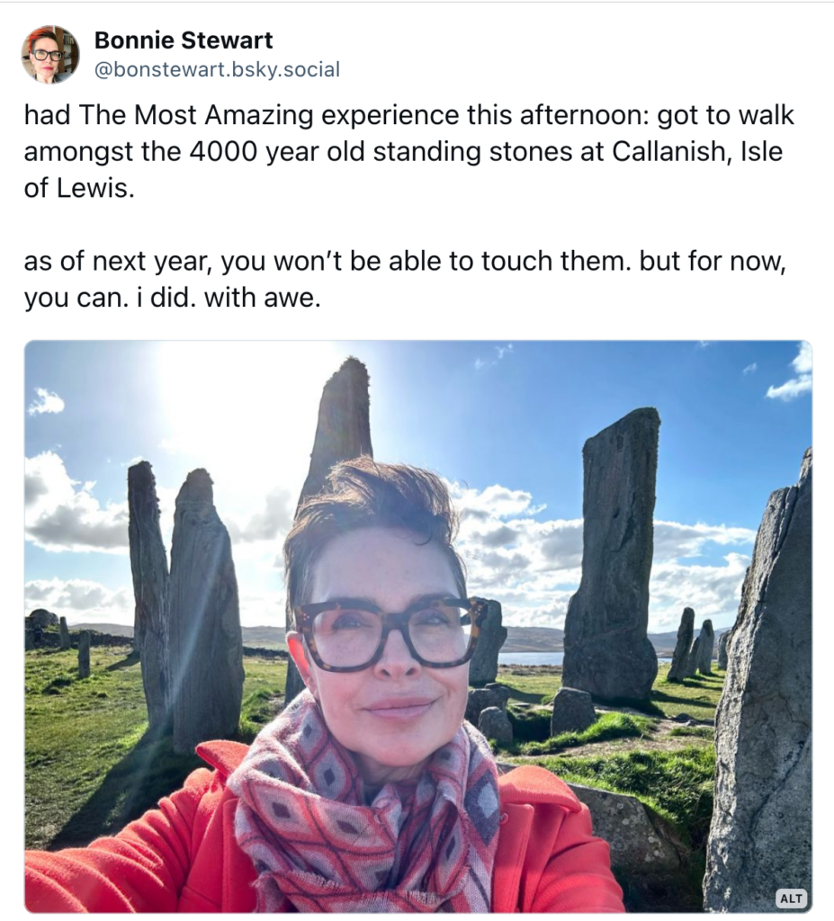 a screenshot from a social media post reads "had The Most Amazing experience this afternoon: got to walk amongst the 4000 year old standing stones at Callanish, Isle of Lewis.

as of next year, you won’t be able to touch them. but for now, you can. i did. with awe."

picture shows a femme person with short hair, glasses, and an orange coat, standing in front of 5000 year old standing stones